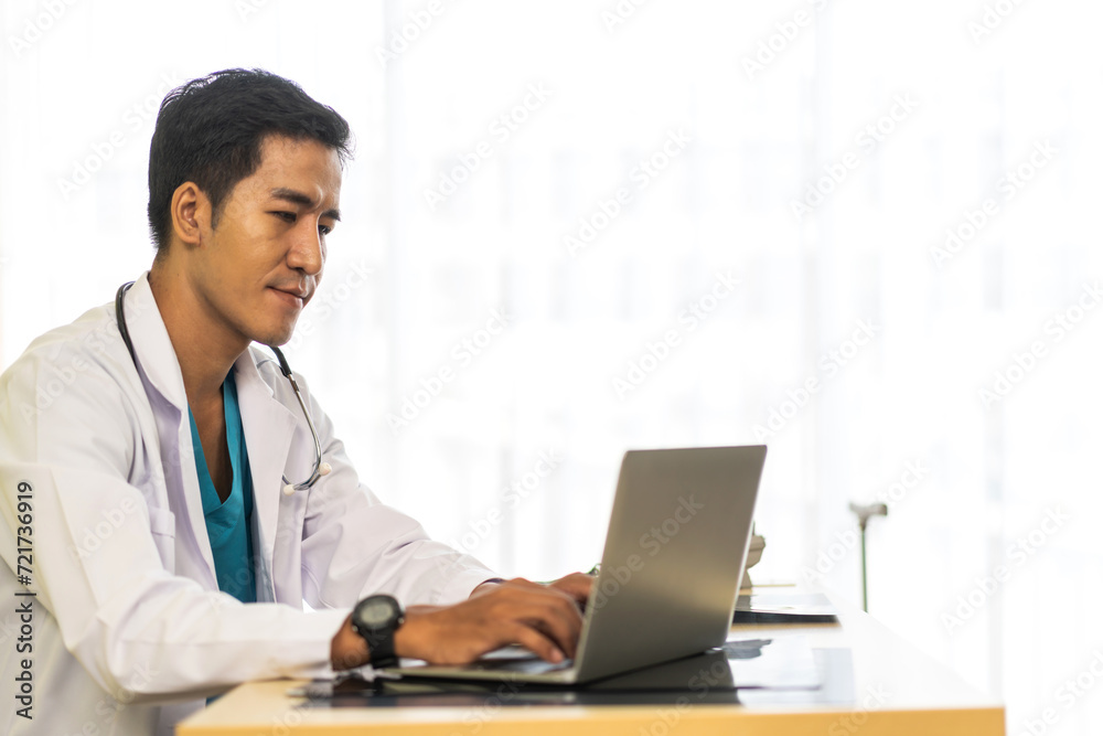 Asian man doctor wearing uniform with stethoscope working with laptop computer with virtual screen medical technology in hospital.healthcare technology and medicine Asian man doctor wearing uniform with stethoscope working with laptop computer with virtual screen medical technology in hospital.healthcare technology and medicine