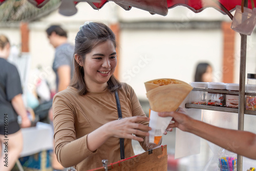Happy young Asian Traveler foodie woman order Crepes at outdoor night market street food vendor photo