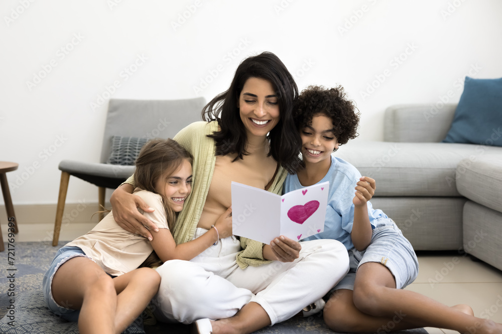Happy Latin mom hugging adorable son and daughter with love, gratitude, holding greeting card with drawn heart, smiling, laughing, celebrating birthday, mothers day Happy Latin mom hugging adorable son and daughter with love, gratitude, holding greeting card with drawn heart, smiling, laughing, celebrating birthday, mothers day