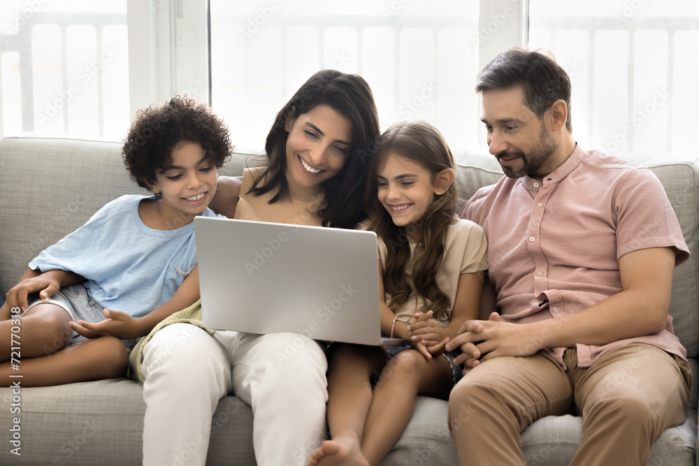 Cheerful Latin couple of parents and two cute kids talking on family group video call at laptop, resting on sofa together, holding computer, enjoying Internet communication, online entertainment Cheerful Latin couple of parents and two cute kids talking on family group video call at laptop, resting on sofa together, holding computer, enjoying Internet communication, online entertainment