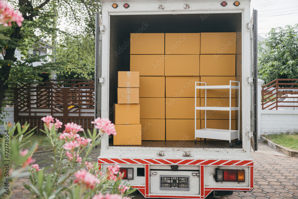 Obraz premium Outdoors a white delivery van and open car trunk carrying moving cardboard boxes. Logistic service for house relocation. Transporting items in crowded truck. Moving Day Concept.