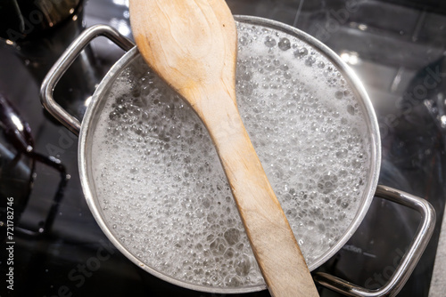 Hot pasta water boiling on a stove with a wooden spoon to prevent boil over.