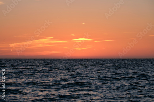 Dramatic bright red sky at ocean sunset  soft evening clouds over sea dark water