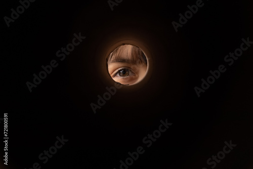What is inside. Curious little kid eye looking into big box through round hall in wall. Cute small child playing hide and seek imagining himself spy peeking watching in peephole from a cover. Close up photo