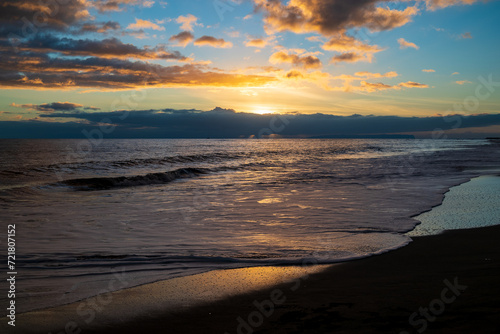 A sunset on Waimea Beach on Kauai reflects warmth onto gentle waves and a glow on the dark sand.