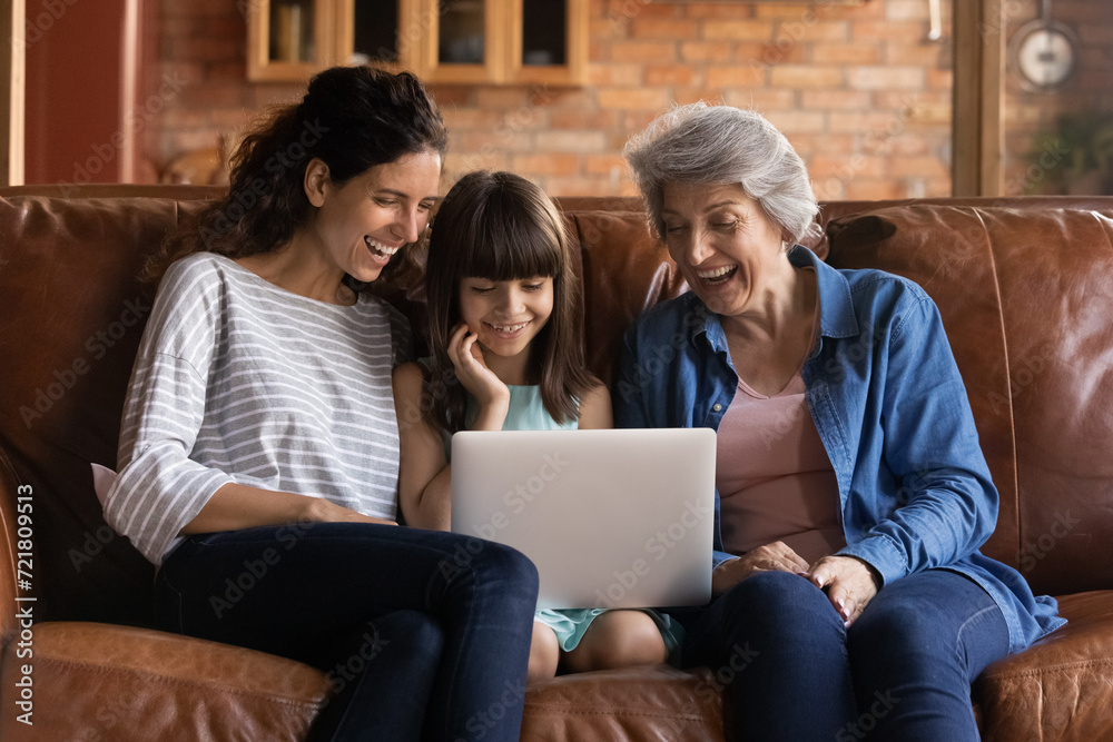 Funny cartoon. Happy intergenerational hispanic family of older grandmother adult mommy and preteen girl daughter grandchild spend free time on couch laugh enjoy cute video movie on laptop computer