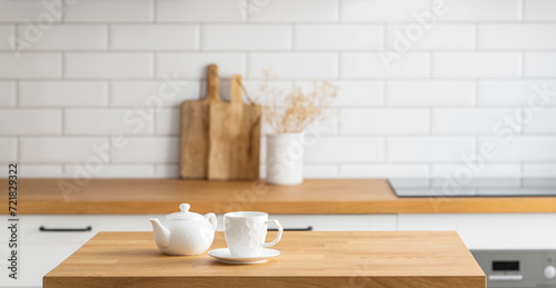 Wooden oak table with a cup of tea and a kettle in front of the kitchen with a white brick background photo