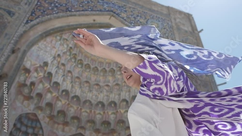 A young woman with long hair in an oriental robe and skullcap stands in the wind near an ancient mosque photo