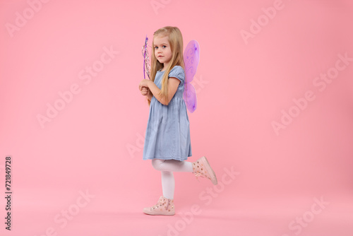 Cute little girl in fairy costume with violet wings and magic wand on pink background