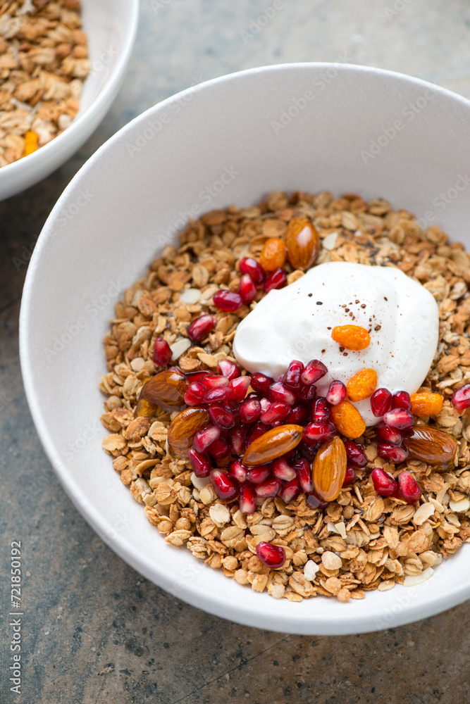 Granola bowl with yogurt, pomegranate seeds, nuts and honey, vertical shot on a beige granite surface, middle close-up, selective focus Granola bowl with yogurt, pomegranate seeds, nuts and honey, vertical shot on a beige granite surface, middle close-up, selective focus