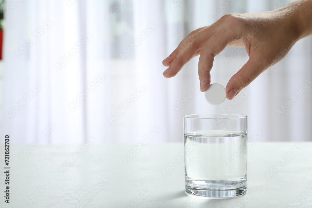Woman putting tablet into glass of water indoors, space for text Woman putting tablet into glass of water indoors, space for text