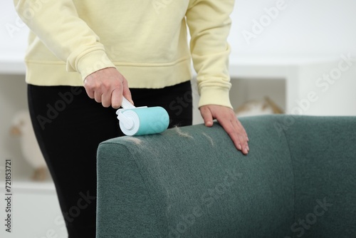 Woman with lint roller removing pet hair from sofa indoors  closeup