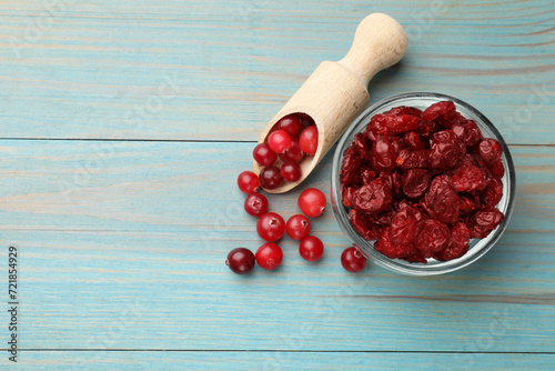 Tasty dried cranberries in bowl and fresh ones on light blue wooden table, top view. Space for text photo