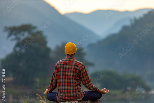 Rear view of man is relaxingly practicing meditation yoga in forest in summer to attain happiness from inner peace wisdom with morning light for healthy mind and soul concept photo