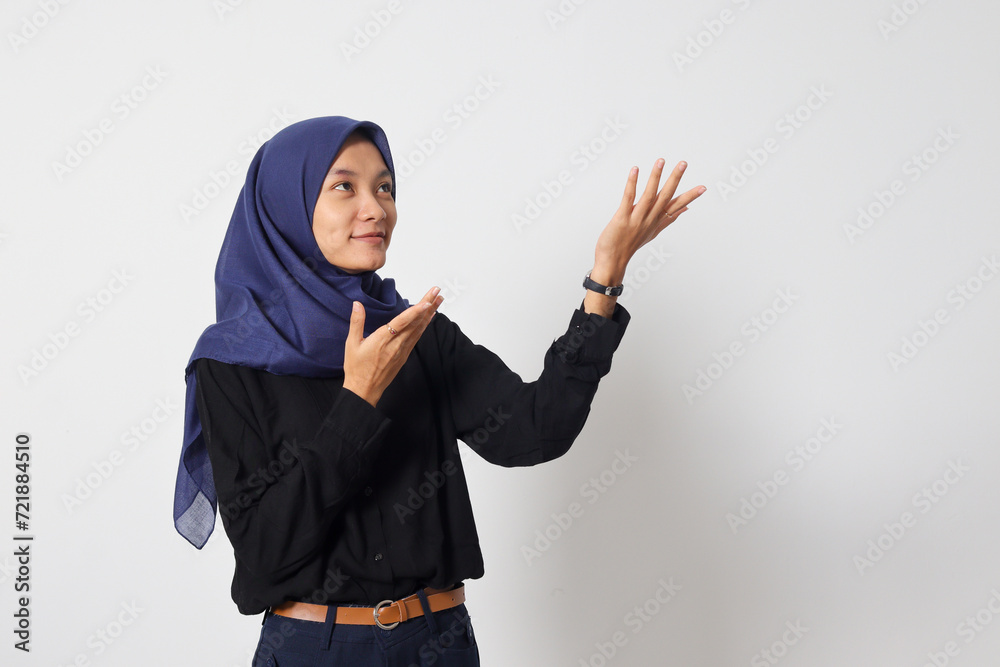 Portrait of excited Asian hijab woman in casual shirt promoting product, pointing finger to the side. Advertising concept. Isolated image on white background Portrait of excited Asian hijab woman in casual shirt promoting product, pointing finger to the side. Advertising concept. Isolated image on white background