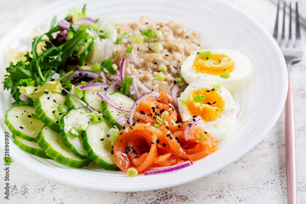 Breakfast oatmeal porridge with boiled eggs, salt salmon, cucumber and red onions. Healthy balanced food. Trendy food.