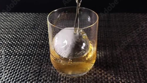 丸い氷を入れたグラスにお酒を注ぐ