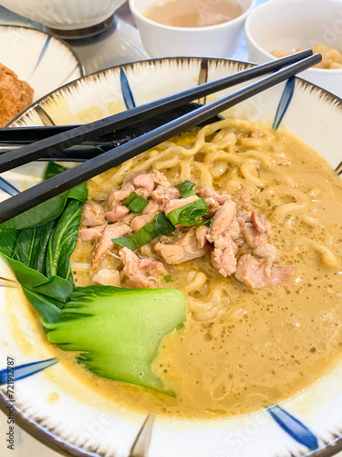 Eating chinese noodle soup topped with dumplings, chicken or beef meat, meatballs, vegetables served in ceramic bowls on a wooden table. photo