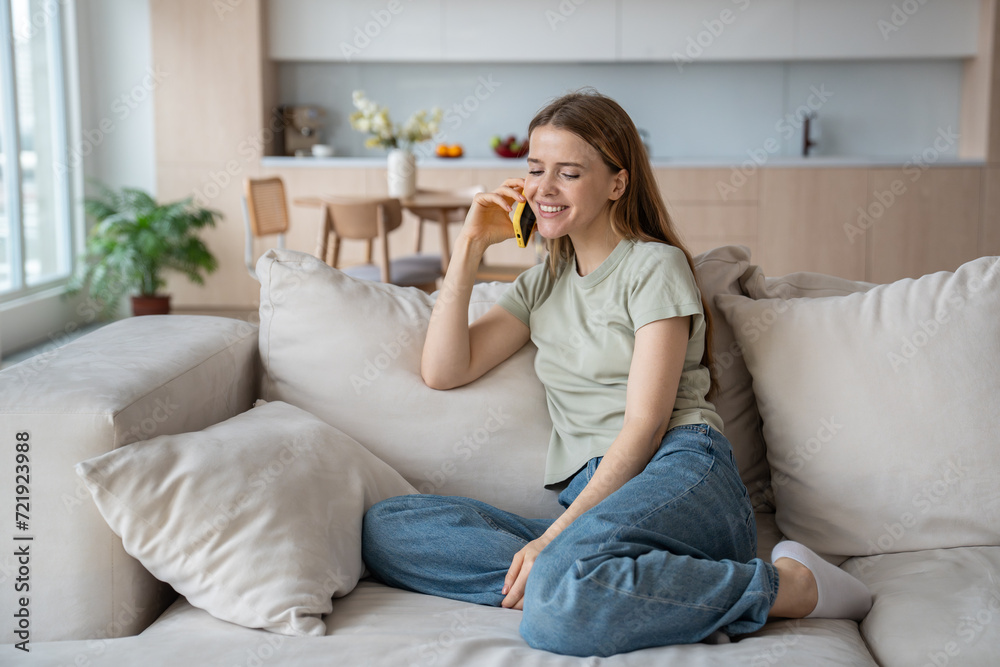 Carefree cheerful merry middle-aged caucasian woman sitting on comfortable sofa at home, speaking over mobile phone, telling, listening to gossips, having pleasant conversation, discussion with friend Carefree cheerful merry middle-aged caucasian woman sitting on comfortable sofa at home, speaking over mobile phone, telling, listening to gossips, having pleasant conversation, discussion with friend