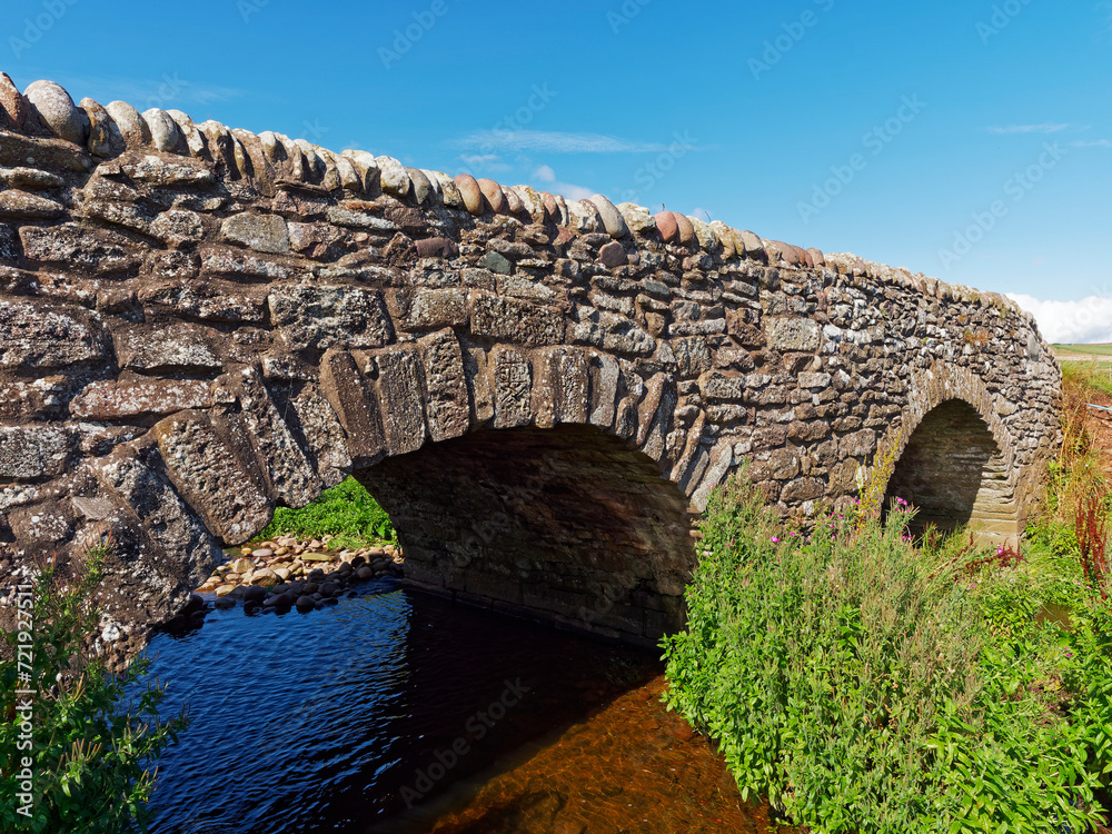 An old restored double arched stone footbridge spanning a small burn at the Haughs of Benholm on the Aberdeenshire Coastal Path.
