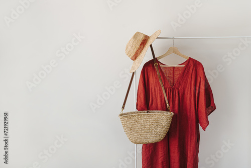 Women's fashion clothes and accessories. Stylish female straw handbag, straw hat, red dress on hanger over white background. Minimalist fashion blog