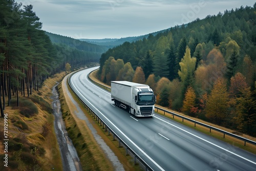 A semi-trailer driving along an asphalt highway through a colorful autumn forest, aerial view. The concept of cargo transportation, logistics.