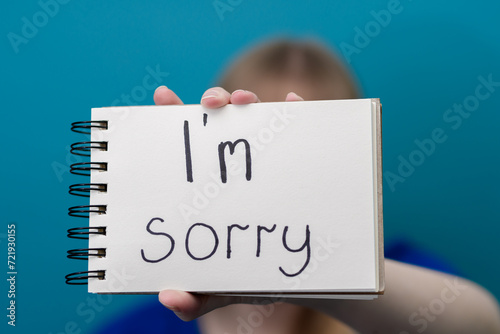 Dziecko trzyma biała kartkę z tekstem, z napisanym odręcznie słowem przepraszam
