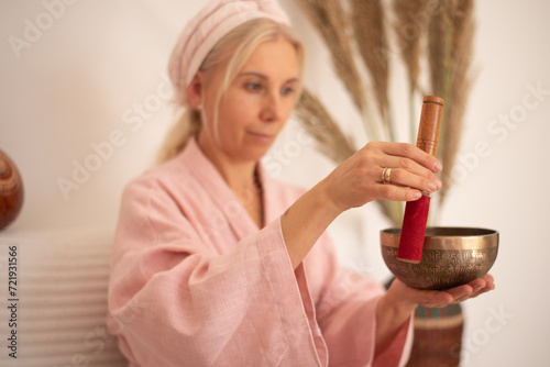 Woman in pink clothes hold metal bells and make music in solon. Indoors. Yoga for health, relaxation and meditation body, practice for forgiveness and spiritual harmony. photo