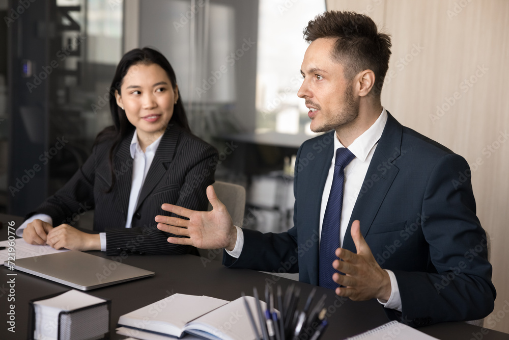 Engaged inspired business professional man offering ideas for team brainstorming, speaking to coworkers at meeting table, explaining marketing plan. Diverse business group working together Engaged inspired business professional man offering ideas for team brainstorming, speaking to coworkers at meeting table, explaining marketing plan. Diverse business group working together