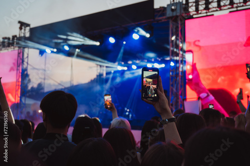 crowd of people at the stage at a live music concert are shooting videos on smartphones in their hands