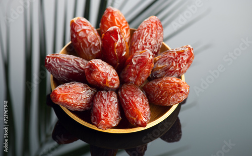 Dates fruit. Date fruits with palm tree leaf reflection on black background. Heap of Medjool dates in wooden bowl close up. Tasty healthy food 