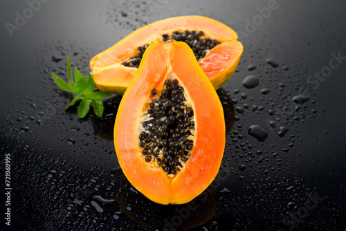 Papaya fruit on wet black background with water drops. Halved fresh organic Papaya exotic fruits with leaf close up. Healthy vegan food 