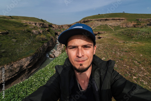 bearded Caucasian male traveler takes a selfie on a smartphone against the background of Aksu Canyon in Kazakhstan in spring © alexkoral