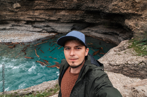 bearded Caucasian male traveler takes a selfie on a smartphone against the background of a river in Aksu Canyon in Kazakhstan in spring