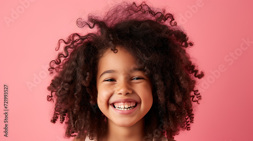 This adorable young girl radiates joy with her curly hair and infectious smile against a vibrant pink background. © stocker