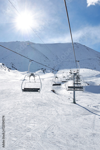 Ski lift with empty chairs at winter resort. Sunny day, blue sky. Snowy Mountain slope. Ropeway construction. Winter vacation activity. Chunkurchak, Bishkek, Kyrgyzstan