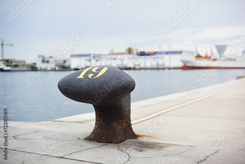 Black marine bollard in harbor with blurred background with ships and industry. photo