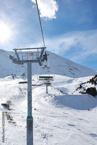 Ski lift pole with empty chairs at winter resort. Sunny day, blue sky. Mountain slope. Ropeway construction. Winter vacation activity. Chunkurchak, Bishkek, Kyrgyzstan