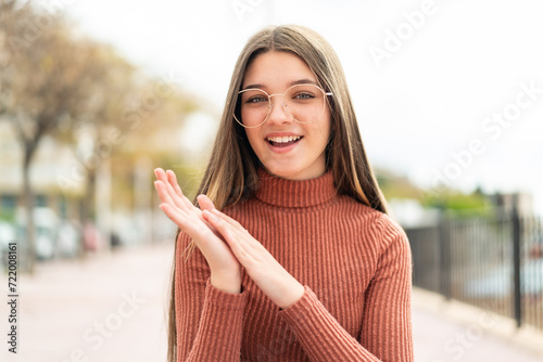 Teenager girl at outdoors With glasses and applauding