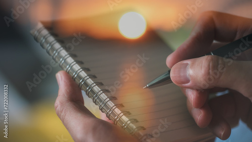 Hand hold pen writing on notebook with blur sunset background in concept of memories travel diary