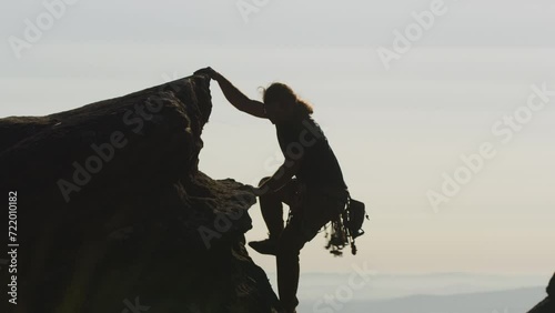 A Long-haired rock climber holding onto a rock and climbing photo