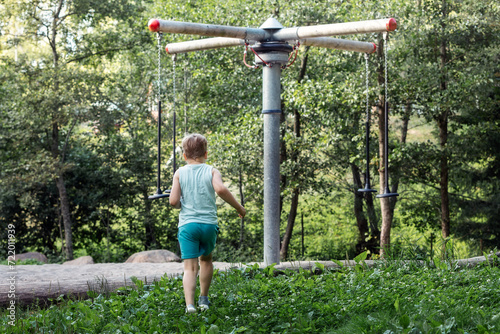 A little boy in blue clothes, photographed from behind, sees a rope carousel in the forest and rushes towards it photo