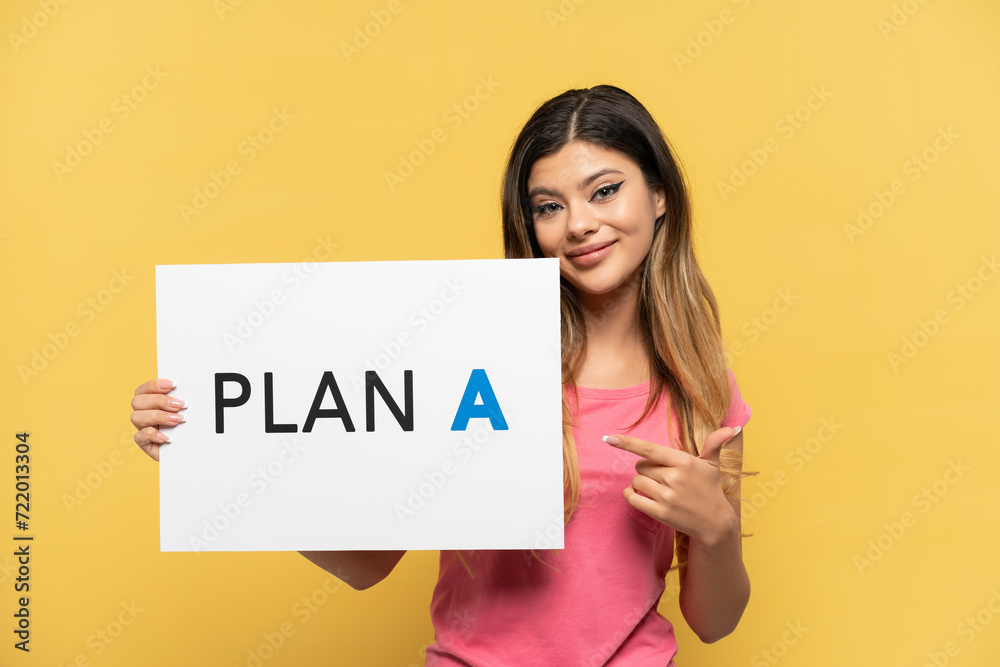 Young Russian girl isolated on yellow background holding a placard with the message PLAN A and pointing it Young Russian girl isolated on yellow background holding a placard with the message PLAN A and pointing it