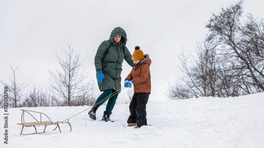 Mother with her son outside in winter with sled