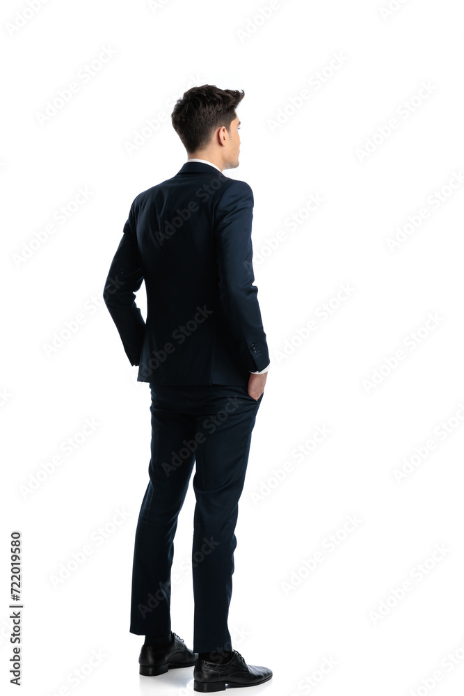 back view of elegant young man holding hands in pockets and standing back view of elegant young man holding hands in pockets and standing