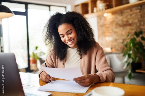 Smiling young black woman sitting at desk working on laptop writing letter in paper notebook, free copy space. Happy millennial female studying using pc. Business And Education Concept