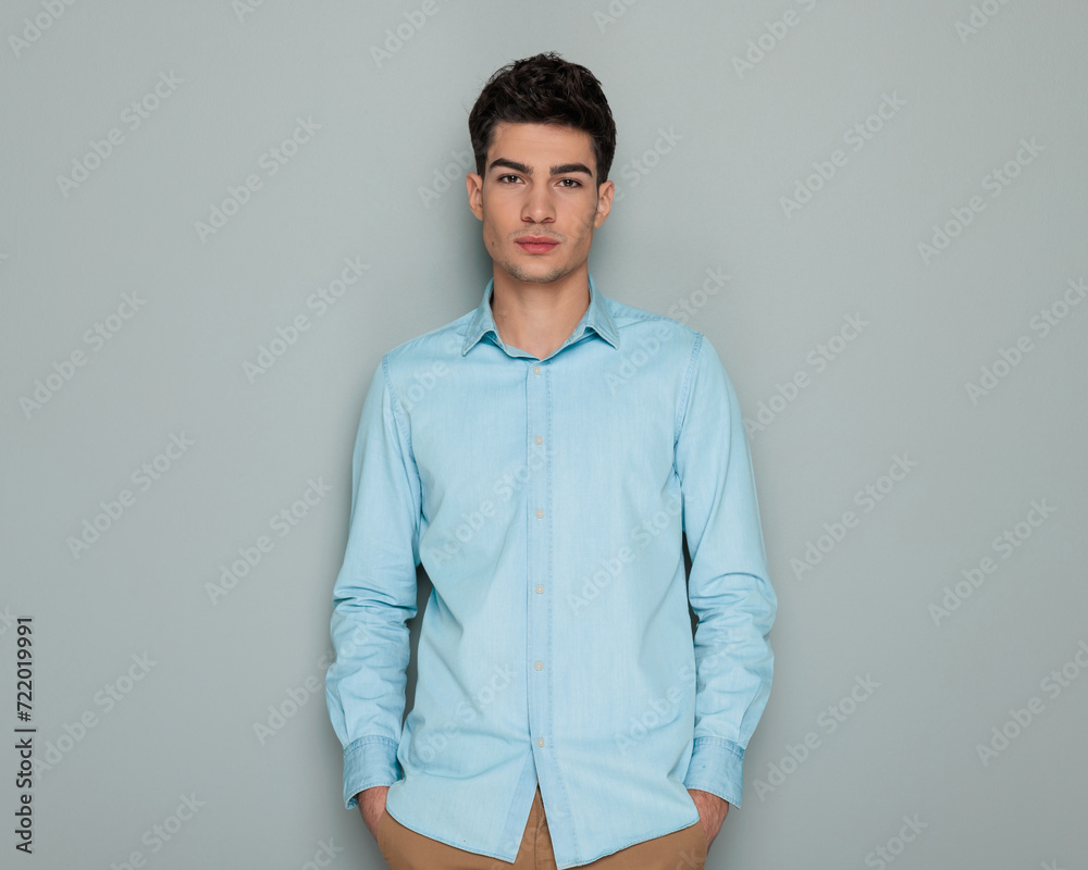 portrait of attractive young man in blue denim shirt holding hands in pockets portrait of attractive young man in blue denim shirt holding hands in pockets