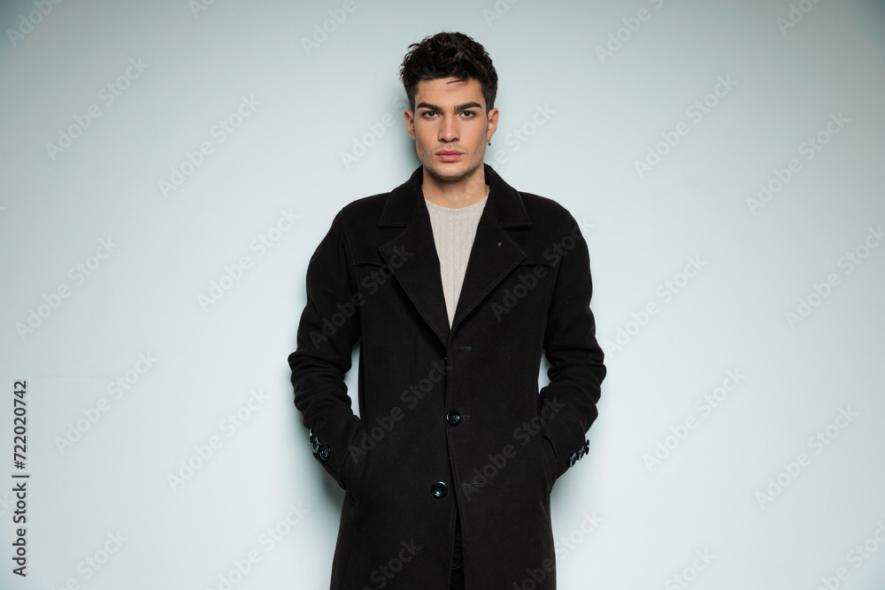 portrait of attractive cool man in black coat holding hands in pockets portrait of attractive cool man in black coat holding hands in pockets