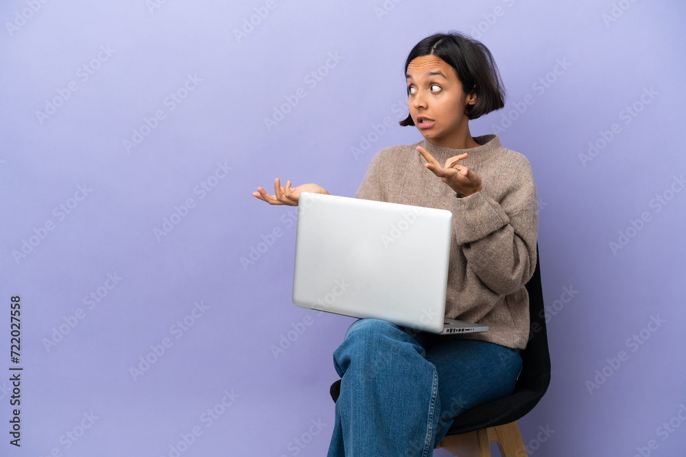 Young mixed race woman sitting on a chair with laptop isolated on purple background with surprise expression while looking side Young mixed race woman sitting on a chair with laptop isolated on purple background with surprise expression while looking side