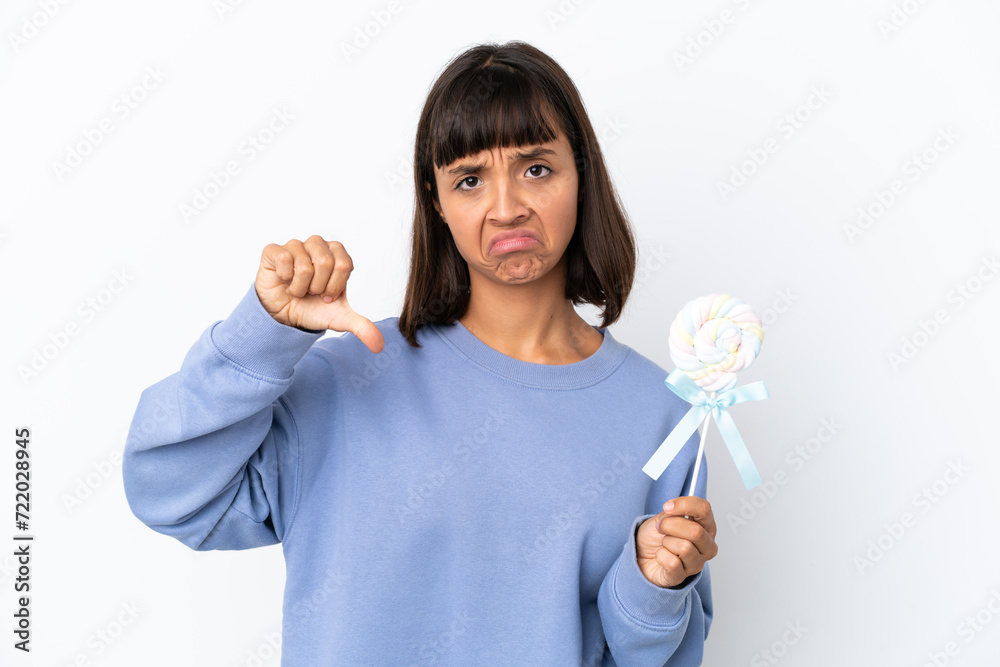 Young mixed race woman holding a lollipop isolated on white background showing thumb down with negative expression Young mixed race woman holding a lollipop isolated on white background showing thumb down with negative expression